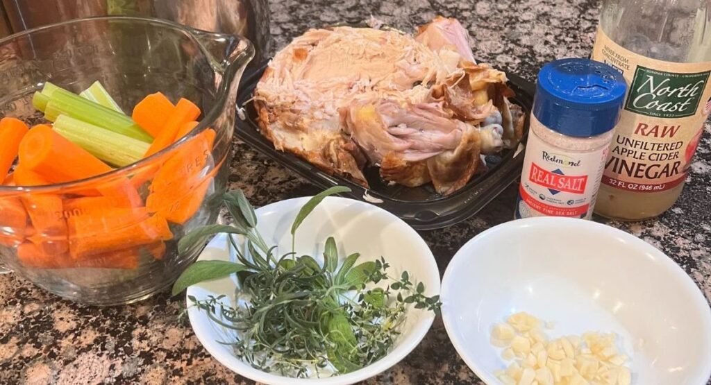 "Fresh ingredients for chicken stock including chicken, carrots, celery, onions, and herbs on a kitchen counter"