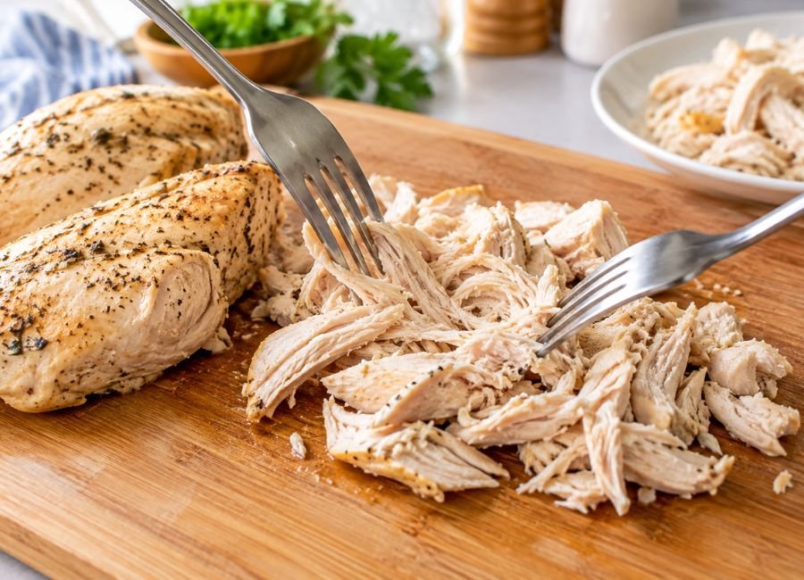 Fully cooked chicken breast being shredded with two forks for chicken noodle soup